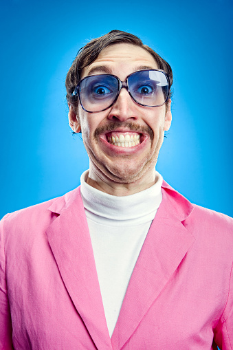 A funny looking salesman with a mustache, blue tinted glasses and a pink blazer with a sickeningly silly grin on his face.  Vertical on teal blue background.