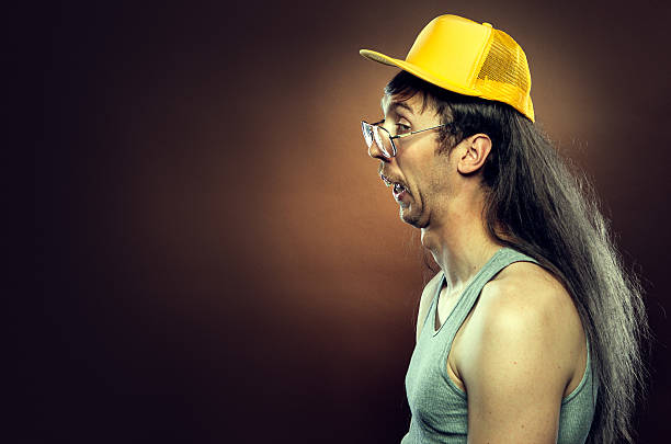 Goofy Redneck With Mullet A profile portrait of a hillbilly man with a long flowing mullet, mustache, trucker hat,  and rotten teeth.  Brown background; horizontal with copy space. mullet haircut photos stock pictures, royalty-free photos & images