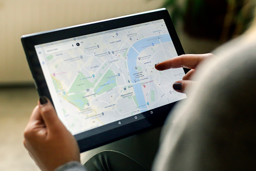 Unrecognizable Caucasian woman using the Google Maps app on a Lenovo tablet, looking at a map of London, UK..