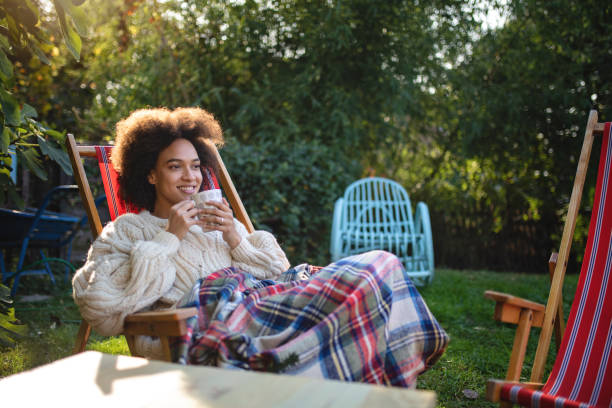 Gorgeous smiling woman enjoying a cup of tea Lovely and serene mixed ethnicity woman enjoying a spring day outdoors in a back yard, sitting on a lounge chair and drinking tea. curley cup stock pictures, royalty-free photos & images