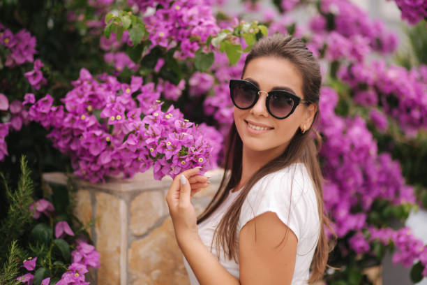 prachtige vrouw in zonnebrillen staan in prachtige bloemen. portret van gelukkig glimlachte jonge vrouw - fluisterboot stockfoto's en -beelden