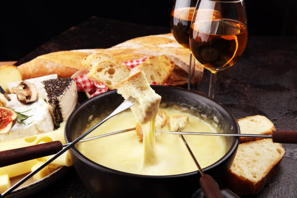 Gourmet Swiss fondue dinner on a winter evening with assorted cheeses on a board alongside a heated pot of cheese fondue with two forks dipping stock photo