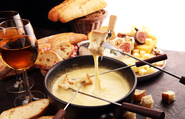 Gourmet Swiss fondue dinner on a winter evening with assorted cheeses on a board alongside a heated pot of cheese fondue with two forks dipping stock photo