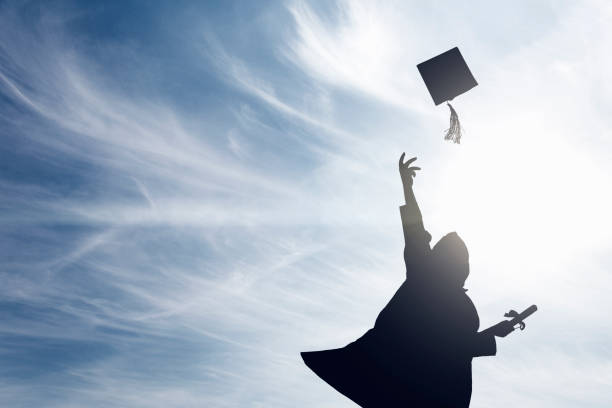 graduate students tossing up hats over blue sky - traje académico imagens e fotografias de stock