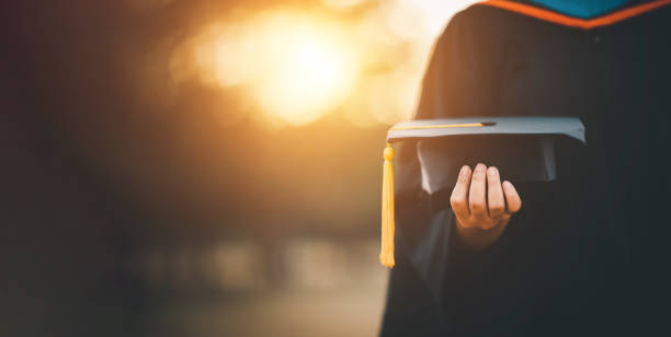 graduates holding black hats with yellow tassels standing with raised diploma in hand over sunset,Concept education congratulation. Graduation Ceremony ,Congratulated the graduates in University. stock photo