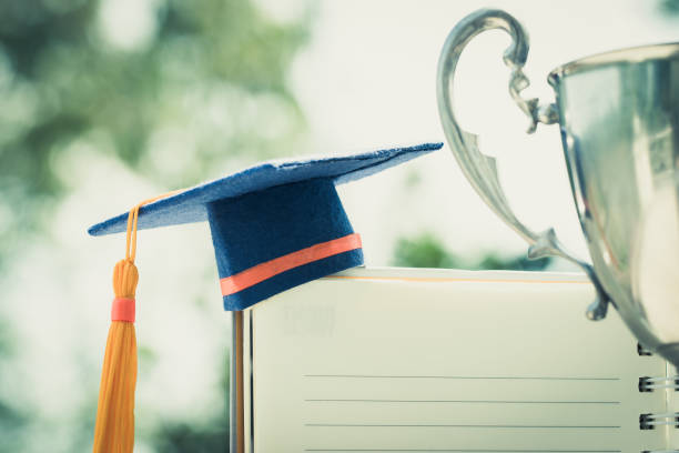 Graduation cap on white notebook with champion trophy show success in education learning study international abroad stock photo