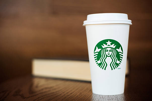 Grande Starbucks to go cup on wooden table with book stock photo
