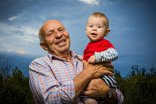 Grandfather Holding Grandson Grandfather holding grandson outdoors, against a sunset sky, smiling. beneficiaries stock pictures, royalty-free photos & images