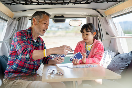 Grandfather playing cards with his granddaughter in a camper van. Kyoto, Japan