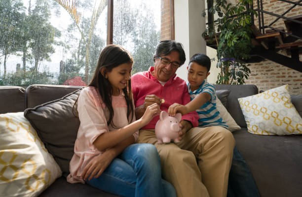 Grandfather teaching his grandkids to save money in piggy bank while sitting on couch at home Grandfather teaching his grandkids to save money in piggy bank while sitting on couch at home all smiling allowance stock pictures, royalty-free photos & images