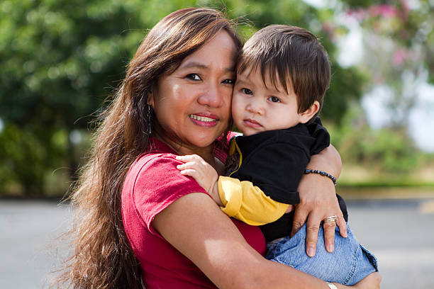 Grandma Hugging Child This young looking Filipino grandmother is hugging her grandson outside in the warm sunshine of Hawaii. neicebird stock pictures, royalty-free photos & images