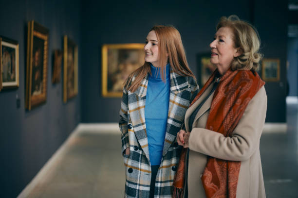 Grandmother and adolescent granddaughter are looking at the paintings in the art gallery. stock photo