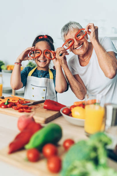 grandmother and granddaughter playing with vegetables - grandparents vertical imagens e fotografias de stock