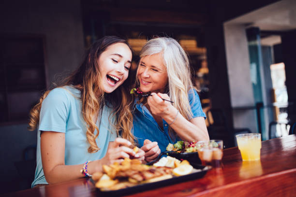Grandmother and teenage granddaughter eating a meal at a restaurant Smiling senior mother and adult daughter sharing lunch at a modern restaurant in the city wundervisuals stock pictures, royalty-free photos & images