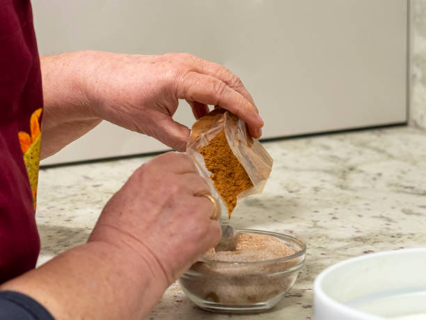 Grandmother mixing cinnamon powder in a bowl with sugar for baking a dessert. stock photo