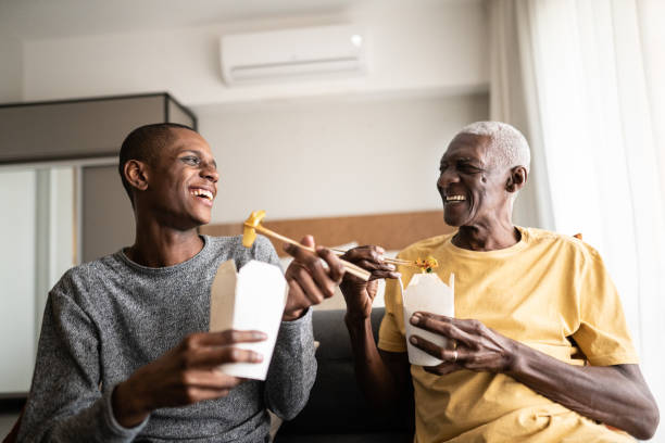 petit-fils et grand-père parlant et mangeant de la nourriture à emporter à la maison - african america man eating chinese food photos et images de collection