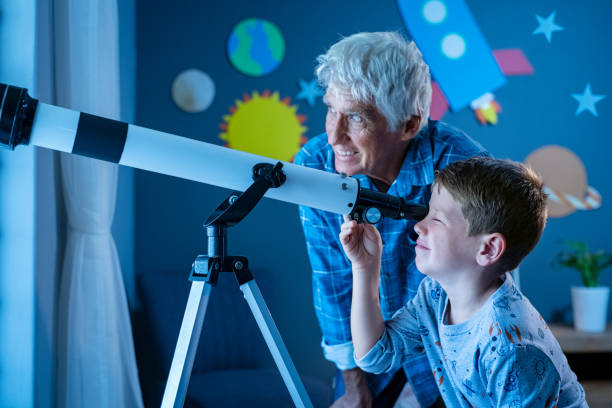 Grandson with grandfather stargazing at night with a telescope Grandfather teaching grandson using telescope to see planets and galaxy. Child watching stars through a telescope at night with senior man. Grandpa and grandchild looking together at their positive future: growing, investment and vision concept. astronomy telescope stock pictures, royalty-free photos & images