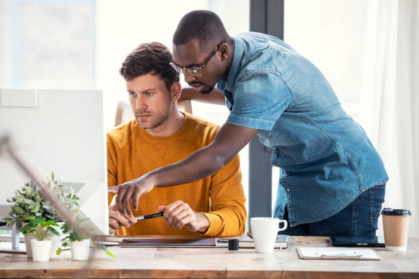 Graphic designer working with computer while showing his job to his colleague in modern startup office. stock photo