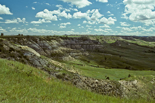 Grassy Canyon and Cloud Formation Theodore Roosevelt National Park lies where the Great Plains meet the rugged Badlands near Medora, North Dakota, USA. The park's 3 units, linked by the Little Missouri River is a habitat for bison, elk and prairie dogs. The park's namesake, President Teddy Roosevelt once lived in the Maltese Cross Cabin which is now part of the park. This picture of a prairie grassland was taken from the Scenic Loop Drive. jeff goulden scanned film stock pictures, royalty-free photos & images