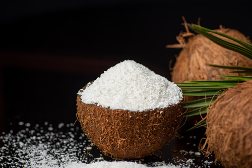 Grated coconut powder falling out of a coconut shell on dark background with copy space