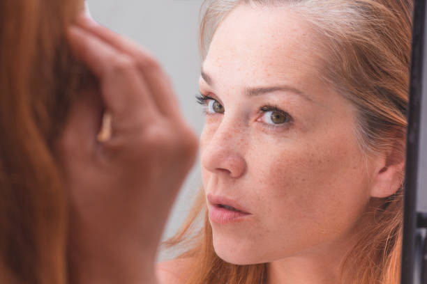 Gray haired woman looking at reflection in morror Gray haired surprised caucasian middle aged woman looking at grey hair head in mirror reflection hair regrowth stock pictures, royalty-free photos & images