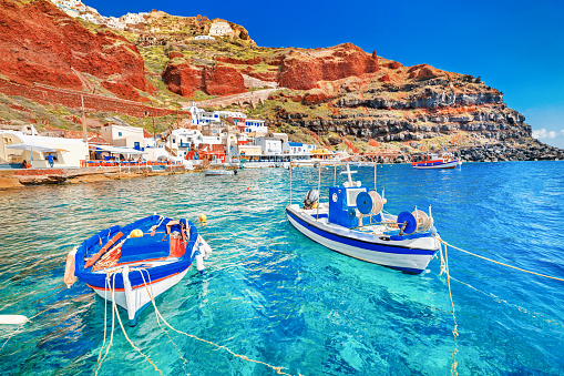 Greece. Breathtaking beautiful landscape of two fishing boats anchored to quay in fascinating blue water at the amazing old port panorama in Oia Ia village on Santorini Greek island in Aegean sea.