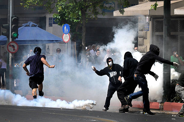Greece in crisis  Athens, Greece -May 05, 2010: Tear gas bombs explodes next to protesters with covered faces who throw stones at riot police during clashes in central Athens, May 05, 2010.    riot stock pictures, royalty-free photos & images