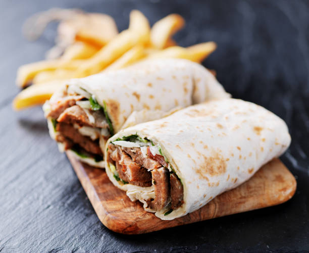 greek gyro wrap cut in half and served with fries greek gyro wrap cut in half and served with fries on simple table shawarma stock pictures, royalty-free photos & images