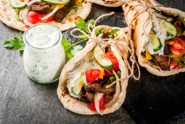 Greek wrapped sandwich gyros Healthy snack, lunch. Traditional Greek wrapped sandwich gyros - tortillas, bread pita with a filling of vegetables, beef meat and sauce tzatziki. On black stone table Copy space shawarma stock pictures, royalty-free photos & images