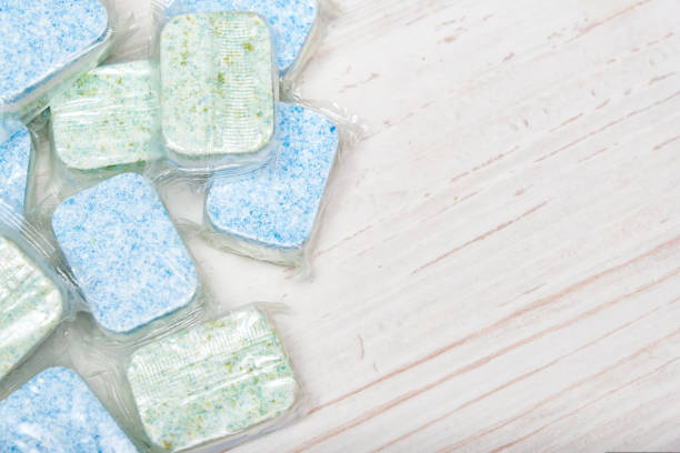 Green and blue dishwasher soap tablets in water-soluble packaging close up on the table with copy space stock photo