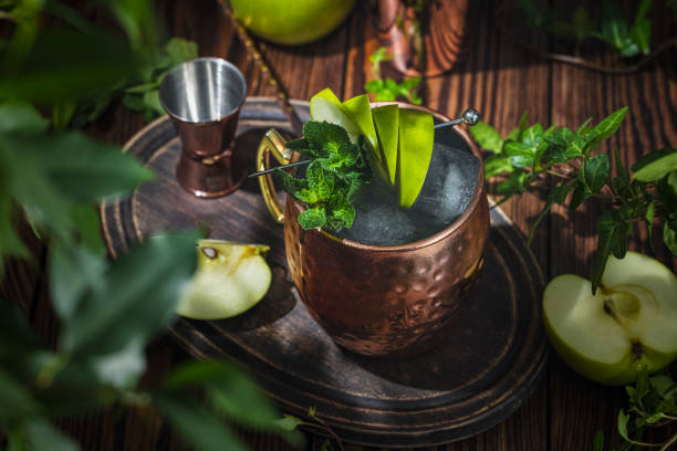 Green Apple Irish Mule. Copper mug filled with Green Apple Irish Mule cocktail or mocktails surrounded by ingredients and bar tools stock photo