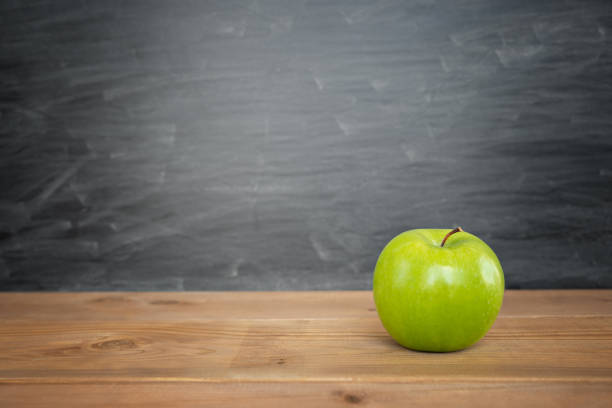Green apple is on a wooden table and chalk board on the back with copy space as back to school or educational concept stock photo
