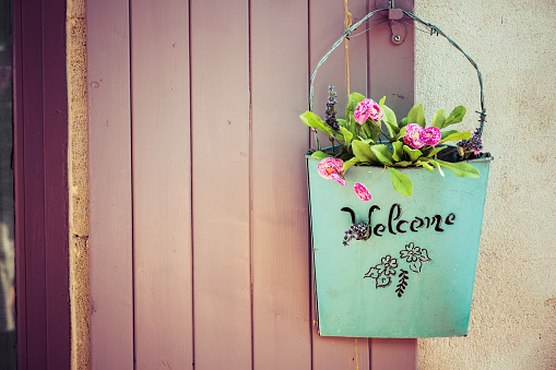 loseup of green basket with fresh flowers and welcome sign text written in black on wall near door