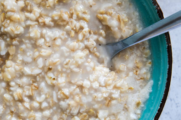 A green bowl of cooked oats porridge with a spoon close up, healthy breakfast and dieting product close up stock photo