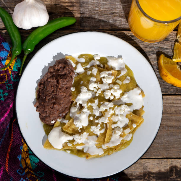 Green chilaquiles with refried beans and cheese on wooden background. Mexican food stock photo