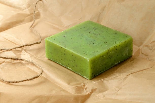 Green handmade herbal soap bar on a brown wrapping paper. Natural toiletries and hygiene products with herbs and essential oils. stock photo