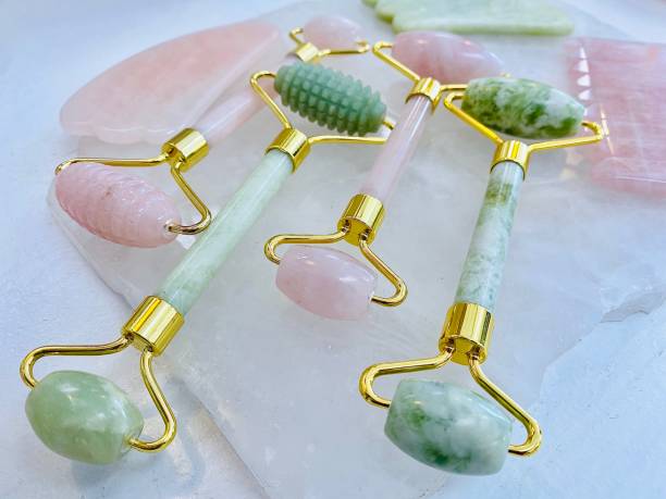 Green Jade and Rose Quarts Rollers Horizontal still life close up of green jade and pink rose quarts crystal facial beauty rollers and combs on crystal rock gua sha tools stock pictures, royalty-free photos & images
