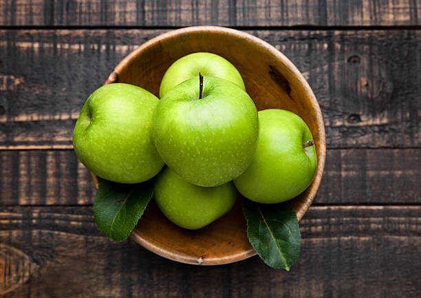 apel sehat organik hijau dalam mangkuk di papan kayu - apel hijau potret stok, foto, & gambar bebas royalti