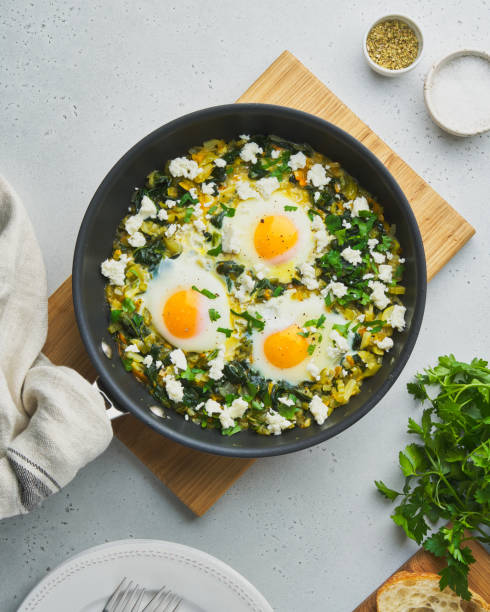 Green shakshouka with eggs, spinach, salty sheep milk cheese, celery and pepper in pan stock photo