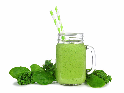 Green smoothie with kale and spinach in a mason jar glass. Side view with ingredients isolated on a white background.