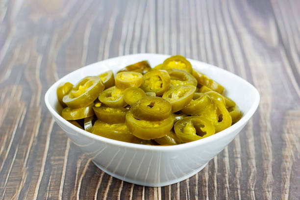 Green spicy sliced marinated jalapeno pepper in white bowl on light background in the kitchen stock photo