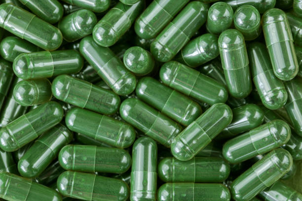 Green Spirulina powder, blue-green algae in clear capsules stock photo