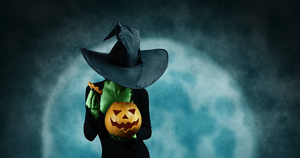 Green witch with pumpkin Green witch opening Halloween carved pumpkin on full moon background. Halloween, horror theme stage costume stock pictures, royalty-free photos & images