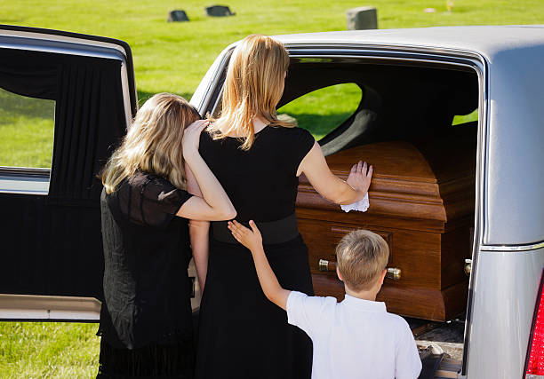 Grieving Family at a Funeral A woman and two children standing behind an open hearse. mourner stock pictures, royalty-free photos & images