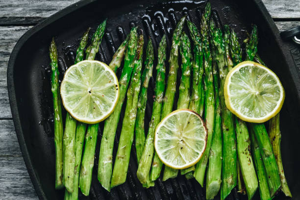 Grilled asparagus. Baked or grilled green asparagus with lemon in black cast iron pan stock photo