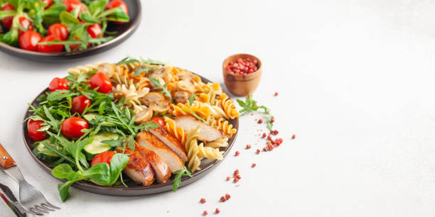 Grilled chicken breast, pasta fusilli, arugula, tomatoes, cucumber slice and mushrooms  in plate. stock photo