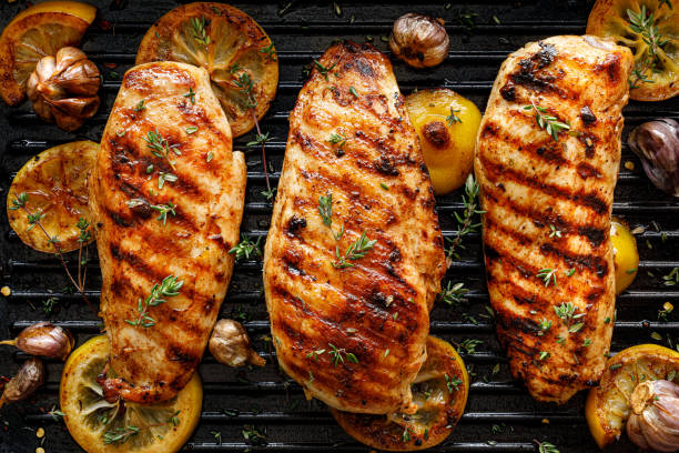 Grilled chicken breasts with thyme, garlic and lemon slices on a grill pan close up stock photo