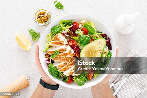 istock Grilled chicken meat and fresh vegetable salad of tomato, avocado, lettuce and spinach. Healthy and detox food concept. Ketogenic diet. Buddha bowl in hands on white background, top view 1295633127