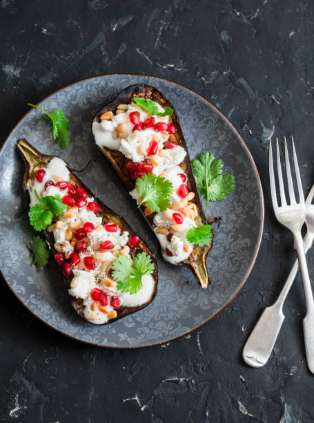 Grilled eggplant with feta, pomegranate, pine nuts and cilantro. Delicious appetizer or snack, on a dark background, top view stock photo