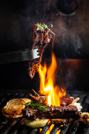 Grilled pork ribs on the grill chopped on a fork against a fire. The cook holds a fork in his hand. concept cooking meat. Close up. place for text.